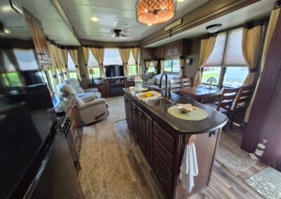 In Kitchen, shows island countertop with sink, refrigerator, kitchen table for four people, and living room in background.