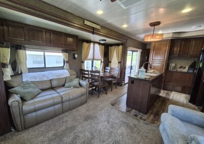 From living room looking toward dining table/kitchen, shows pullout love seat, dining table with four chairs, kitchen island and main sliding door.