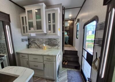 Image from kitchen shows additional counter space with overhead cabinets, main entry door on the right and 3 steps up to main bathroom and bedroom.