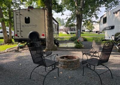 brick fire pit with 4 metal chairs and back of rockwod travel trailer